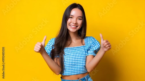 Young Latina woman smiles brightly wearing a checkered blue and white top posing against a vibrant yellow background expressing joy fashion style