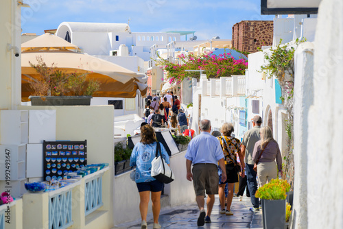 Schilderij op canvas A crowded narrow pedestrian walkway past whitewashed buildings with shops and cafes in the picturesque center of Oia, Greece, on the island of Santorini