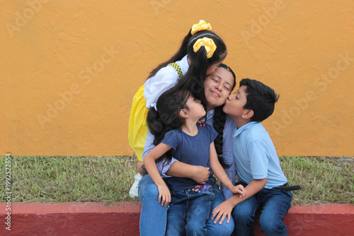 25-year-old Latina mother with her two daughters and son show their love with kisses and hugs to celebrate Mother's Day