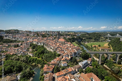 Aerial view of the historic old town featuring St. Nicholas Cathedral, red-roofed buildings, the Sarine river, and the Zaehringen Bridge in Fribourg, Fribourg, Switzerland.
