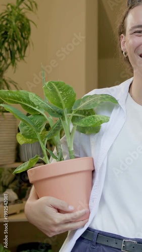 Vertical video: Recording person wearing white T-shirt presenting clay pot in doorway showing plant