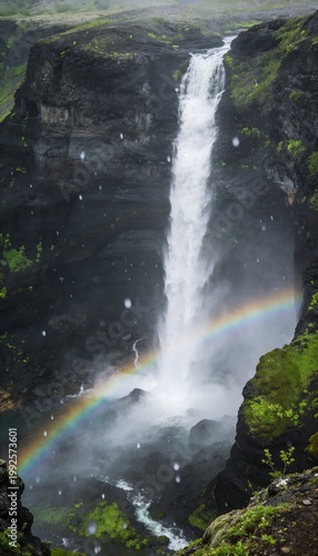 Beautiful waterfall cascading down dark volcanic cliffs with a vibrant rainbow in the mist