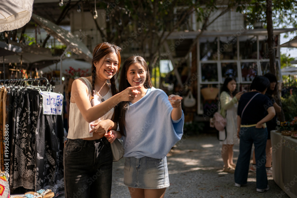 Naklejka premium Young women friends pointing enjoying street market shopping