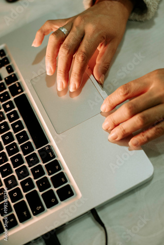 Obraz na płótnie Close-up of hands using a laptop trackpad, soft warm lighting, minimal workspace, focused digital interaction and productivity at home