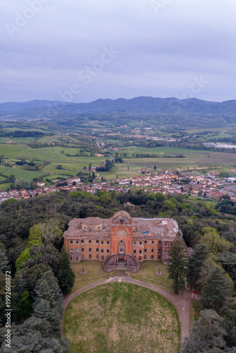 Aerial view of the historic Sammezzano Castle with its unique Moorish Revival architecture surrounded by lush green forests and the rolling hills of Reggello, Tuscany, Italy.