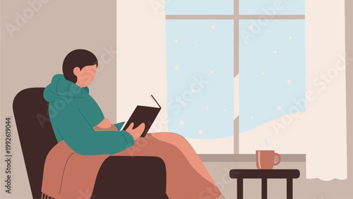 Woman sitting on a chair, reading a book next to a coffee cup on a small table by the window with snowy view outside in a cozy atmosphere.