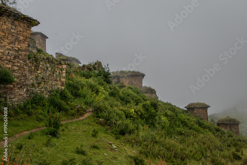 Ancient Stone Houses on Foggy Mountain Path with Lush Green Vegetation