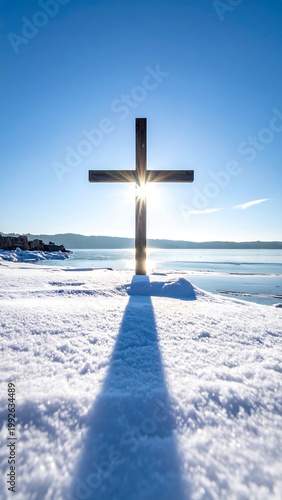 Wooden cross stands in snow, sun shining through. Serene winter landscape