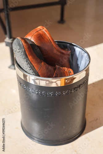 Old leather men's shoes discarded in a trash bin, symbolizing wear and tear, and the passage of time, reflecting on the journey of life and fashion.