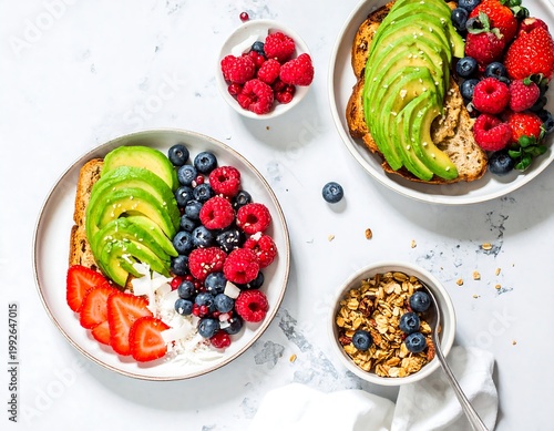 A delicious and healthy breakfast spread featuring avocado toast with fresh berries and granola on a white marble countertop