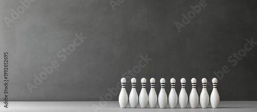 Ten white bowling pins with black stripes standing in a perfect row on a light grey surface against a dark grey background, minimalist still life.