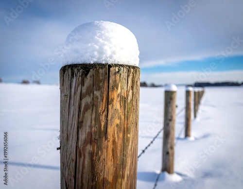 Wooden fence posts covered in snow stretch across a bright, snow-covered field