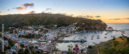 Фотография Panoramic coastal town at sunset with hillside buildings, a curved harbor full of boats, and a prominent round waterfront landmark
