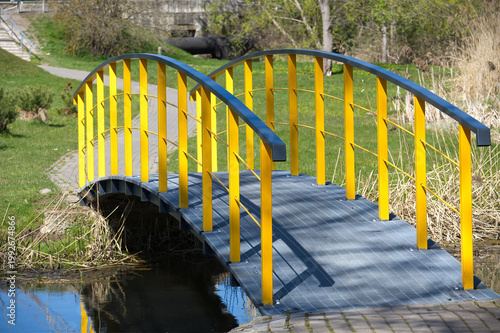 Vibrant yellow pedestrian bridge arches over a calm stream in a park setting