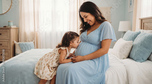 Mother's Day pregnant woman with toddler daughter kissing belly in bedroom expressing sibling love anticipation for lifestyle magazine editorial content