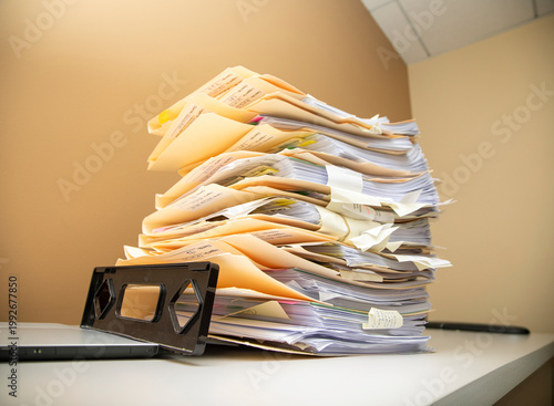 Manila folders stacked overflowing an in box at an office on a white background
