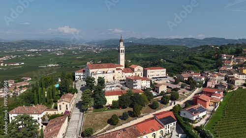 Historical church of Santi Fermo e Rustico in Colognola ai Colli, Italy. Aerial drone shot of the religious landmark and architecture set against the rural Italian landscape and vineyards.