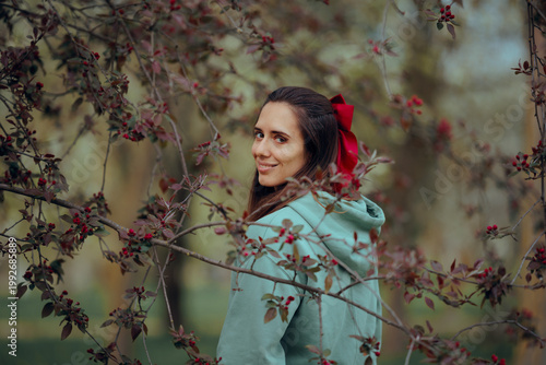Woman with a Red Bow in Her Hair Enjoys Spring Nature. Beautiful lady glancing at the camera looking relaxed and peaceful 