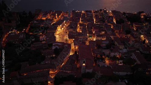Aerial view of Lazise, Lake Garda, Italy, during sunset. Drone footage highlights the old town, medieval walls, and scenic waterfront.