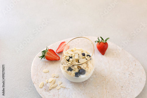 Healthy yogurt parfait with almond flakes blueberries and fresh strawberries on marble tray. High-angle shot features glass bowl with sliced berries highlighting morning wellness routine and organic