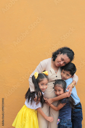 Young, 50-year-old Latina grandmother with brown skin takes care of her grandson and granddaughters, who show their love with hugs to celebrate Mother's Day