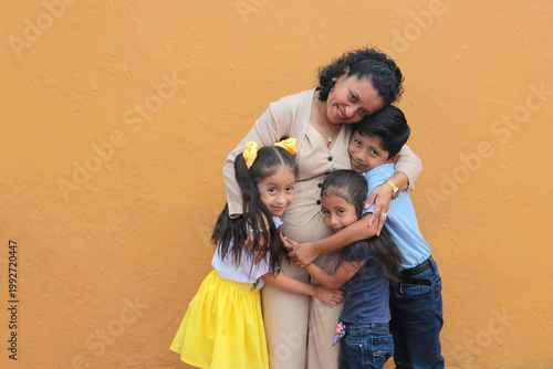 Young, 50-year-old Latina grandmother with brown skin takes care of her grandson and granddaughters, who show their love with hugs to celebrate Mother's Day