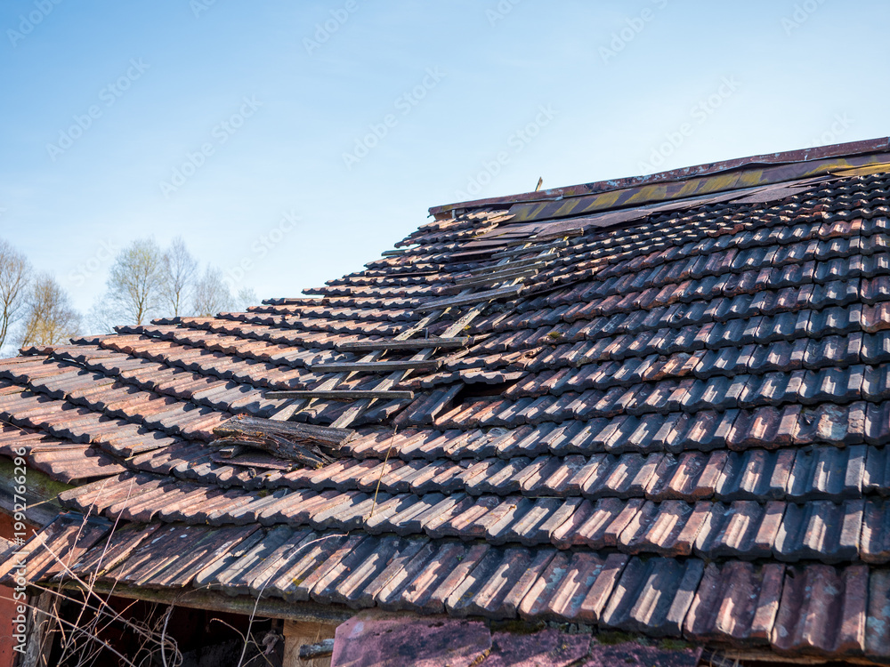 Naklejka premium Old damaged roof with broken concrete tiles and visible structural decay. Concept of house repair, maintenance, renovation, risk and property damage. 