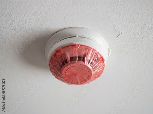 Smoke detector covered with a red plastic dust cover on a white ceiling
