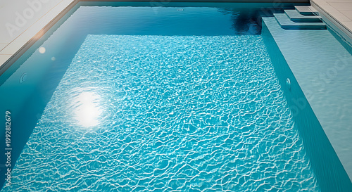 Top down view of a serene minimalist clear blue swimming pool with gentle sunlight reflection on rippling water surface
