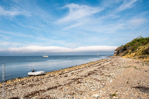 Stony beach with dinghy and anchored sailboats off west coast of Æbelø island in Kattegat, north of Funen, Denmark