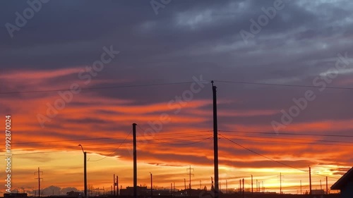 Fiery sunset sky with layered clouds and silhouetted utility poles over horizon in rural landscape