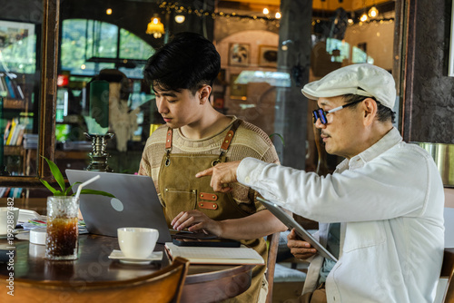 Modern small business digital management young entrepreneur using laptop and tablet planning, finance workflow efficiency technology cafe business operation, learning from senior cafe owner experience