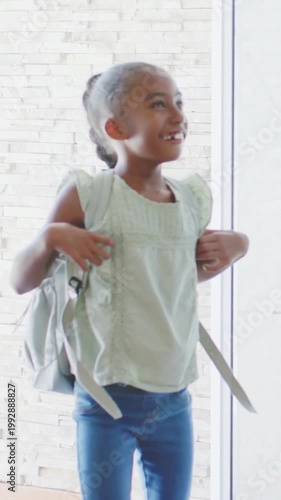 Vertical video: Door opening youth wearing green top and jeans entering foyer, adjusting backpack