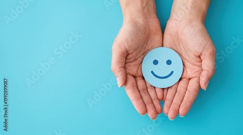 Hands holding a blue smiley face cutout against a bright teal background symbolizing happiness