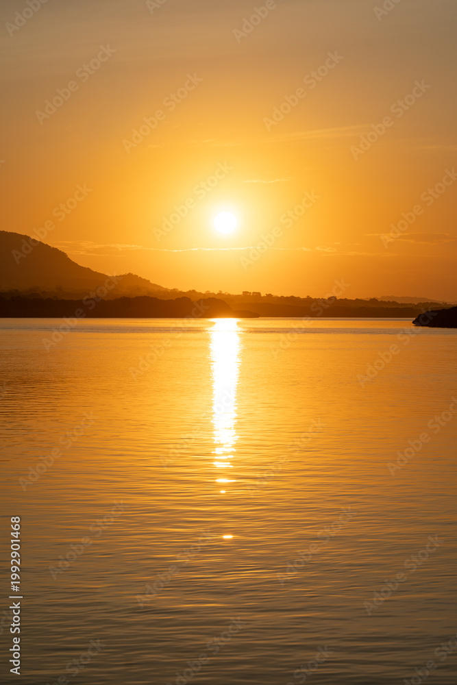 Naklejka premium Panoramic view of a peaceful ocean at dawn during golden hour with bright sun and hazy hills in the distance