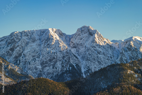 Snow-covered mountains rise in the distance under a clear blue sky during the late afternoon hours in a winter landscape. Giewont, Zakopane