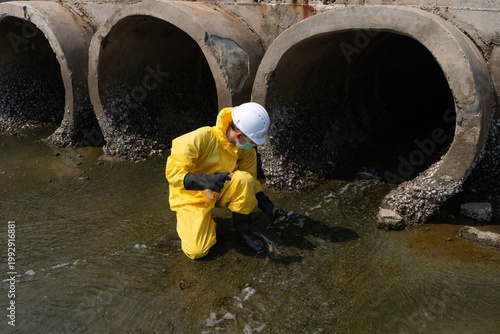 Cuadro en lienzo Environmental engineers, wearing yellow chemical protective suits and helmets, are collecting water samples from sewers to check for pollution and environmental quality