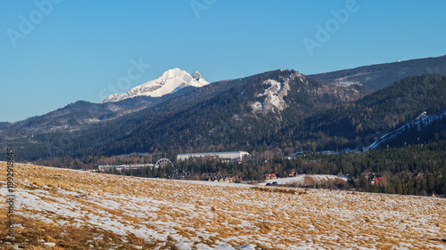 Snow-covered mountains and clear sky over a valley with a small town and amusement park in the distance during winter. Zakopane, Tatra mountains, Poland
