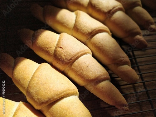fresh golden brown croissants on a metal cooling rack with dramatic side lighting and shadows