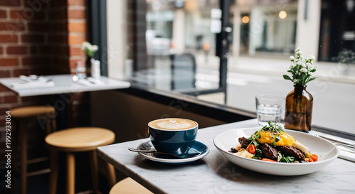 Latte and a plated savory brunch dish served on a marble table by a cafe window