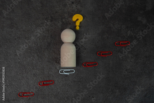 Wooden figure pondering at the base of a staircase of paper clips and question mark