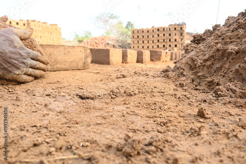 A person manually shaping bricks in an open field. Using a rectangular wooden mold and raw, reddish-brown clay, the worker skillfully forms each brick on the dusty ground. Slow motion video.