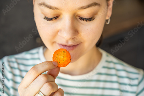 Photos Woman eating carrot chip as healthy snack at home