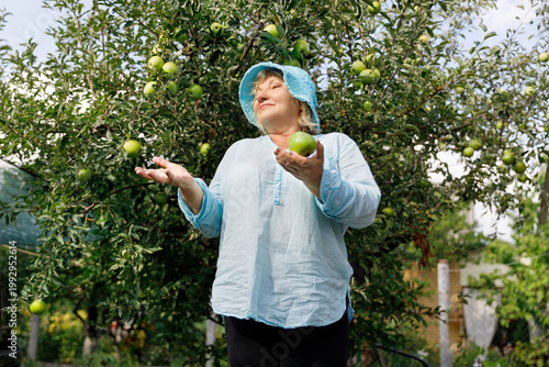 Happy senior woman posing under an apple tree with harvest.