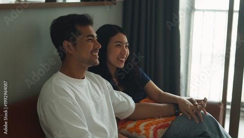 Fotografie Affectionate couple relaxing, holding hands and watching tv while cuddling on li
