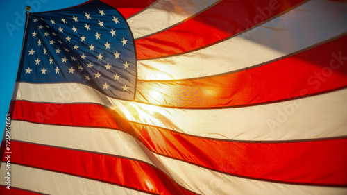 The American flag waves proudly in the wind with sun rays illuminating its fabric against a clear blue sky