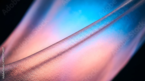 Abstract macro close up of translucent wavy material with pebbly texture illuminated by vibrant pink and blue neon lights for background design.