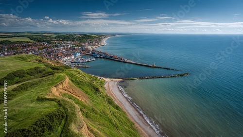 Aerial view from the top of Beeston Bump cliff looking down at Sheringham pier and the colorful coastal town, green grassy foreground, blue North Sea