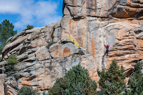 Climber on a granite rock wall in La Pedriza, with forest below and a snow-capped mountain background. A striking scene that captures adventure travel, outdoor exploration, and natural beauty of Spain