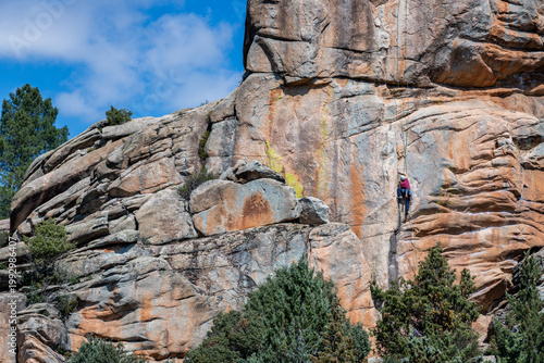 Climber on a granite rock wall in La Pedriza, with forest below and a snow-capped mountain background. A striking scene that captures adventure travel, outdoor exploration, and natural beauty of Spain